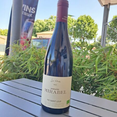 Bouteille de vin rouge Éclat Mirabel avec verres sur fond de bois et vignes cévenoles